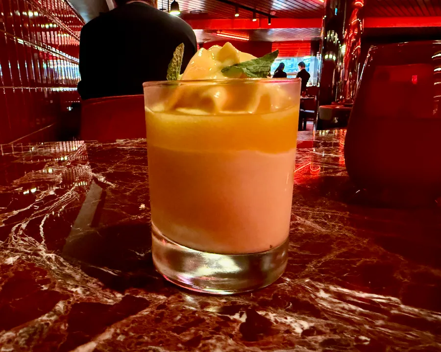 Orange cocktail garnished with mint on a marble bar counter