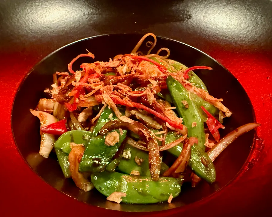 Stir-fried sugar snap peas with crispy shallots in a black bowl