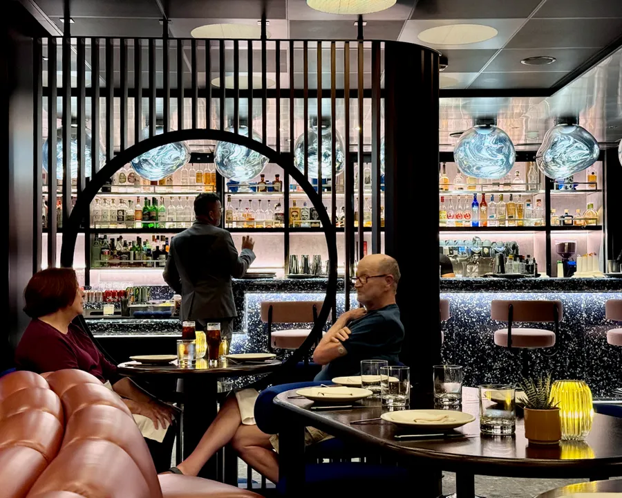 The bar at Pink Agave on Virgin Voyages with bright lights and strictly lined-up bottles 