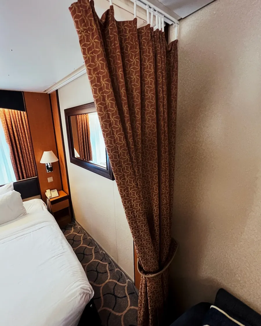 A heavy curtain is shown which separates an ocean view cruise liner cabin bed from the rest of the room