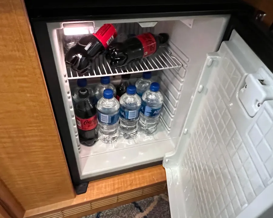 A mini-bar stocked with Coke Zero and bottled water inside a cruise ship cabin