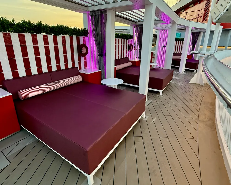Outdoor lounge daybeds with purple cushions and pink lighting on Scarlet Lady deck