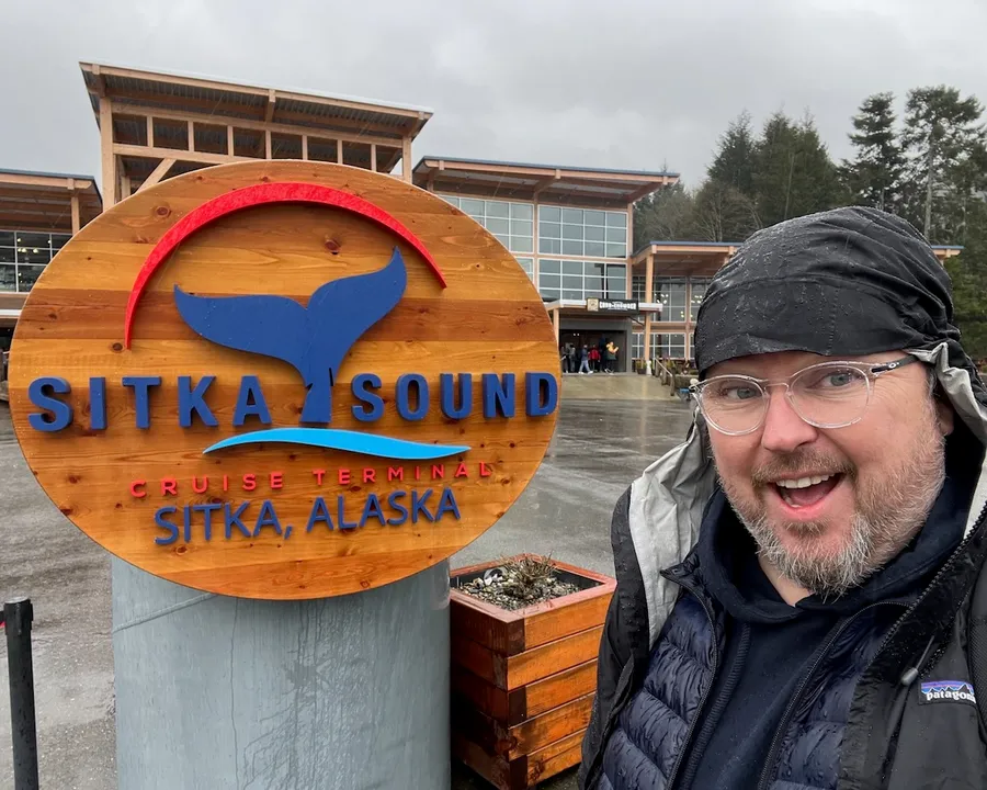Patrick Hughes beside a sign reading Sitka Sound